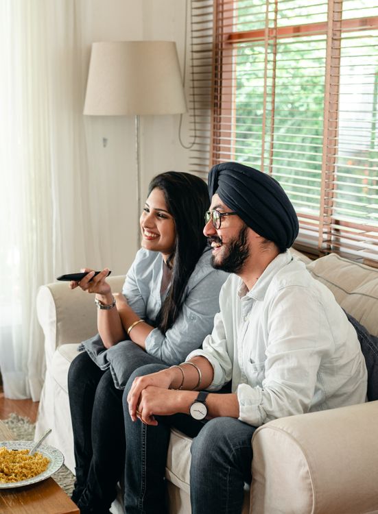 couple souriant sur canapé regardant la TV avec télécommande IPTV